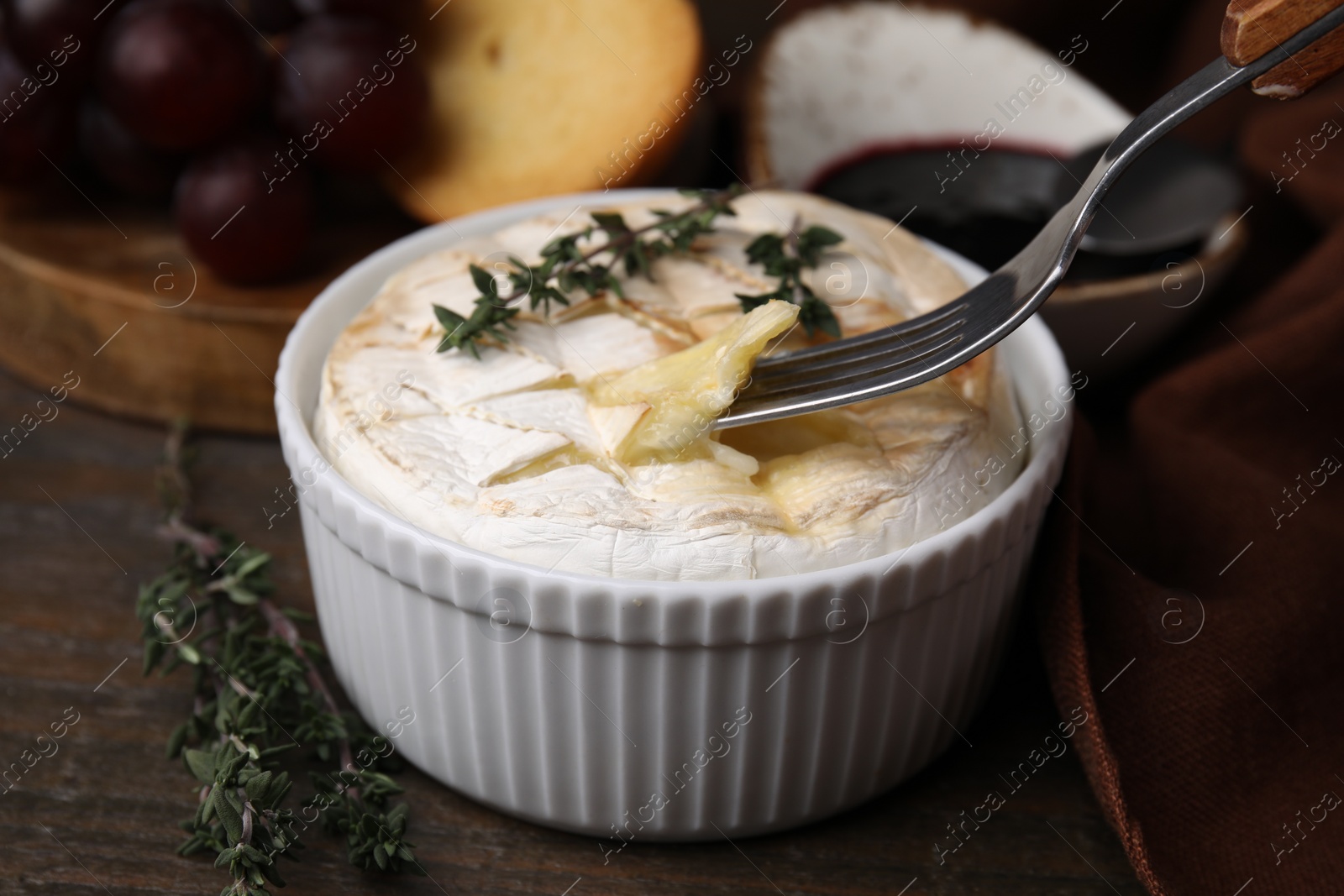 Photo of Eating tasty baked camembert with fork from bowl at wooden table, closeup