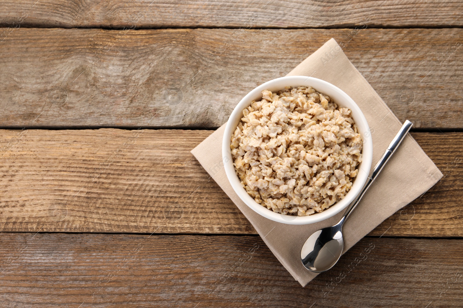 Photo of Tasty boiled oatmeal in bowl and spoon on wooden table, top view. Space for text