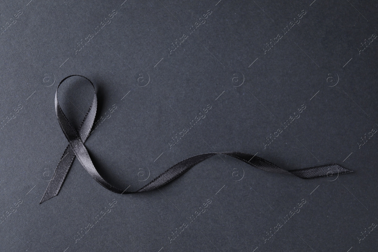 Photo of Black ribbon on dark background, top view with space for text. Funeral symbol