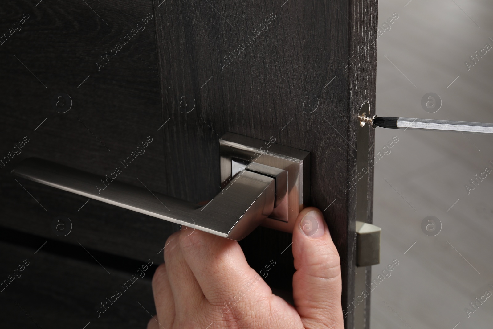 Photo of Handyman with screwdriver repairing door handle indoors, closeup