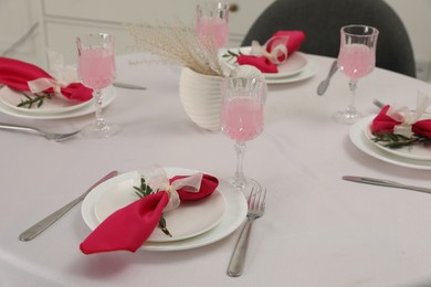 Photo of Color accent table setting. Glasses, plates, cutlery and pink napkins on table