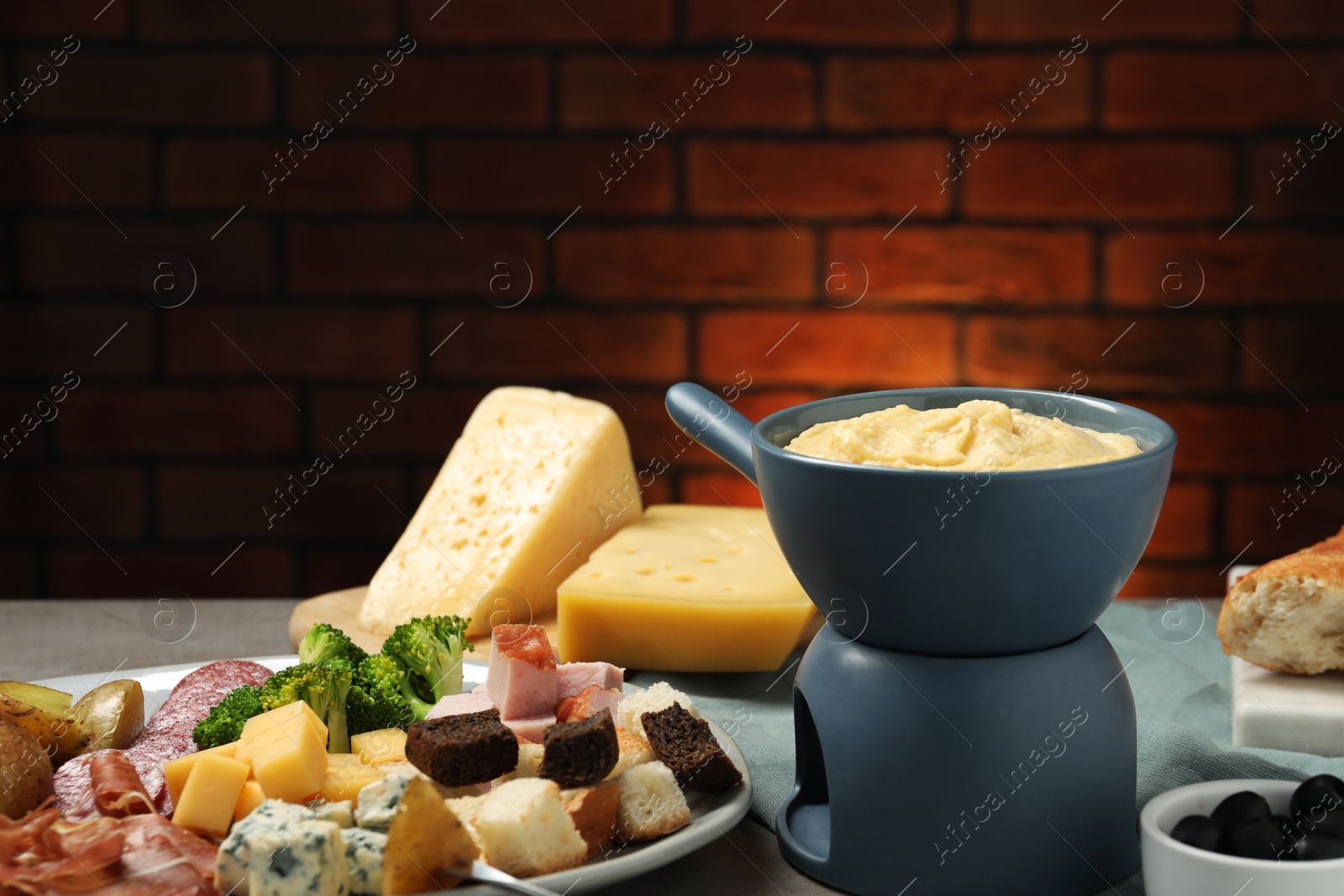 Photo of Tasty melted cheese in fondue pot and snacks on table, closeup