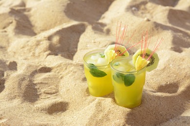 Photo of Glasses of refreshing drink with kiwi and mint on sand. Space for text