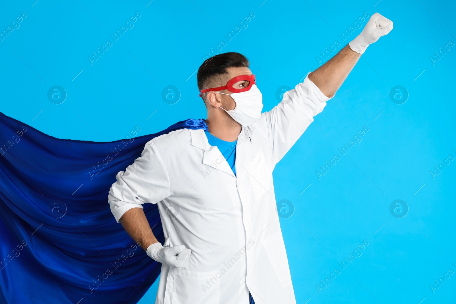 Photo of Doctor wearing face mask and cape on light blue background. Super hero power for medicine