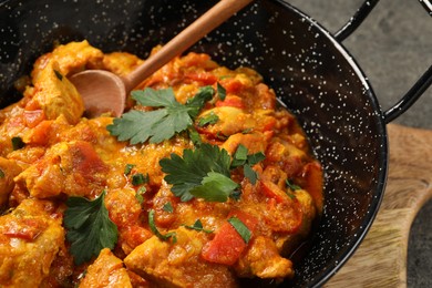 Photo of Delicious chicken curry in frying pan and spoon on table, closeup