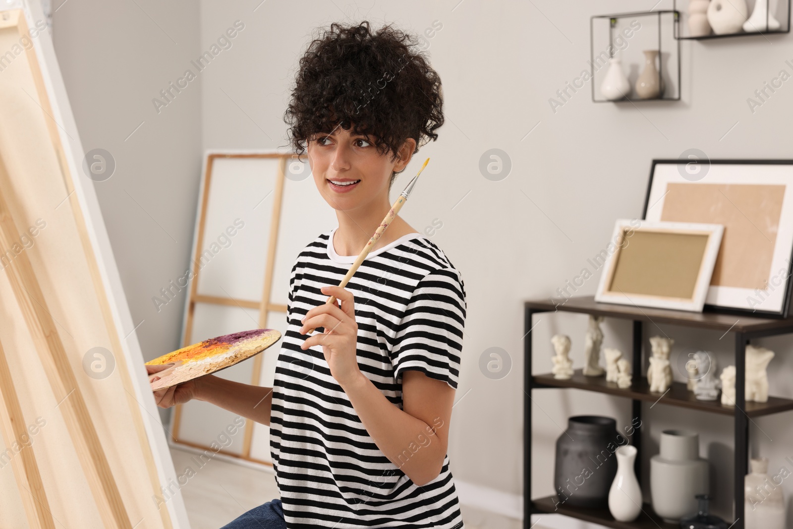 Photo of Young woman painting on easel with canvas in studio