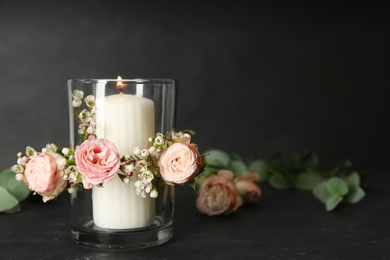 Photo of Glass holder with burning candle and floral decor on black stone table. Space for text
