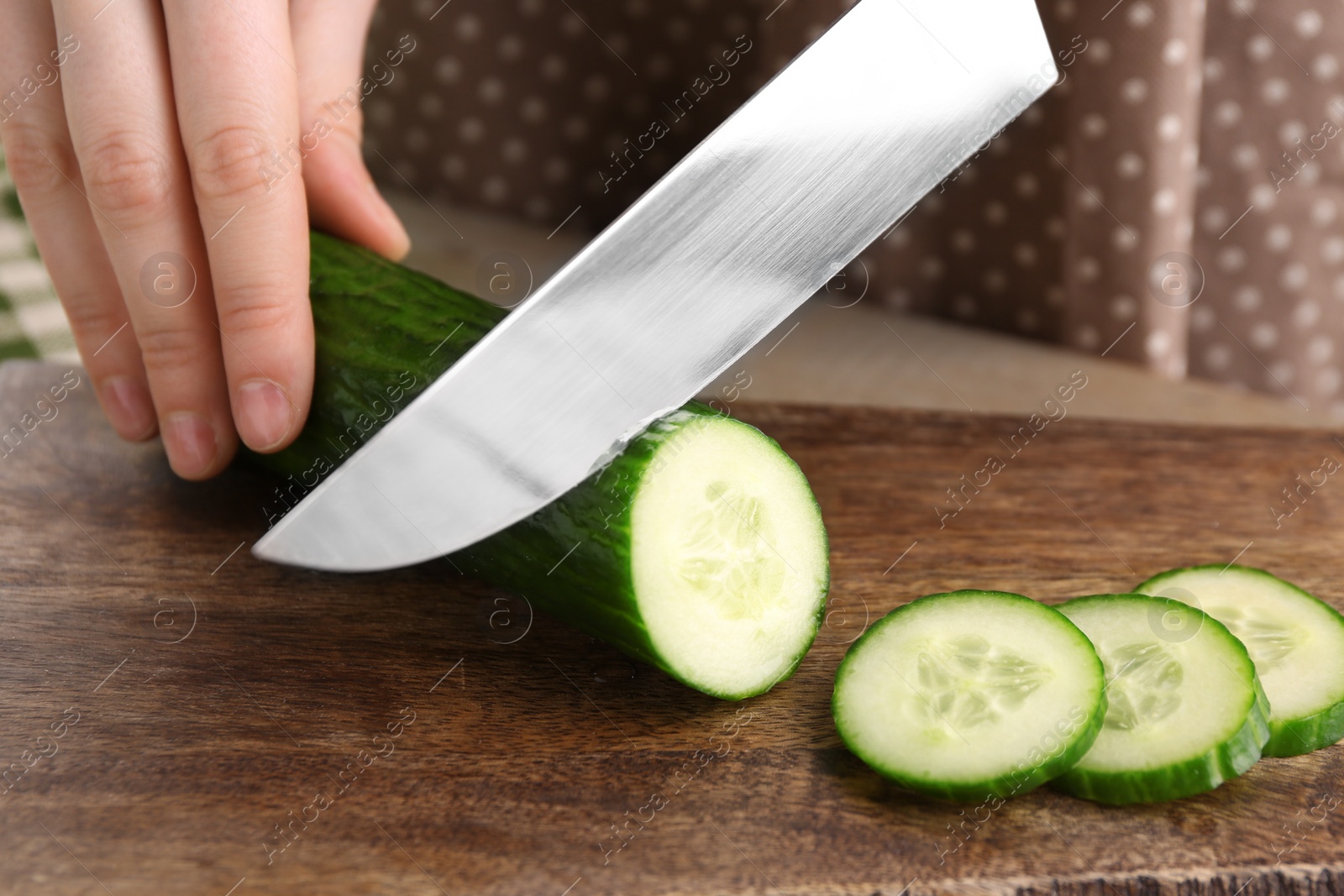 Photo of Woman cutting cucumber on wooden board, closeup