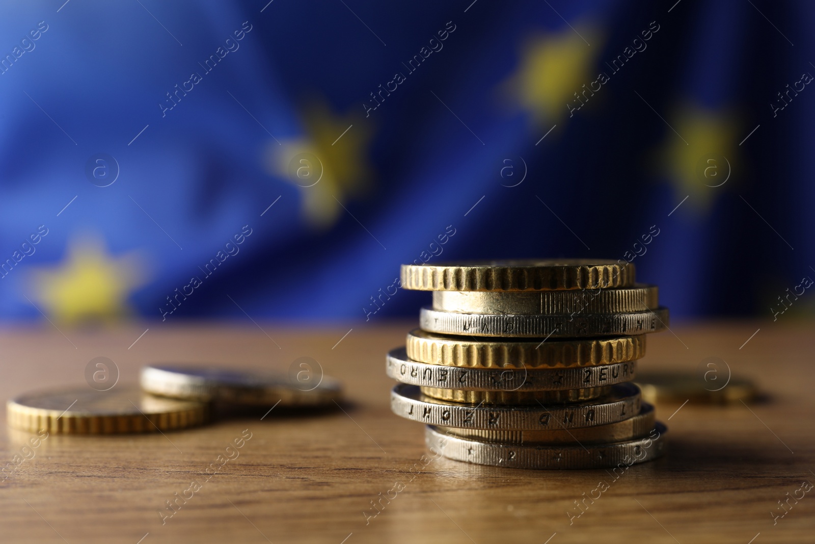 Photo of Coins on wooden table against European Union flag, closeup. Space for text