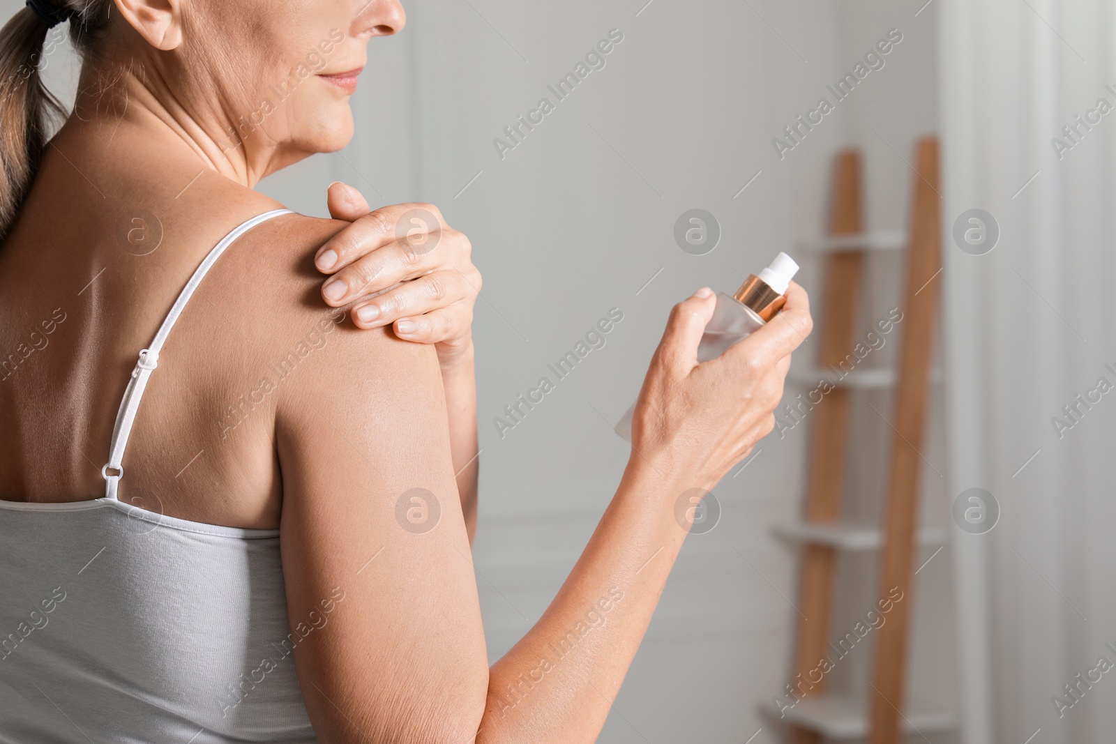 Photo of Happy woman holding bottle of body oil indoors, closeup. Space for text