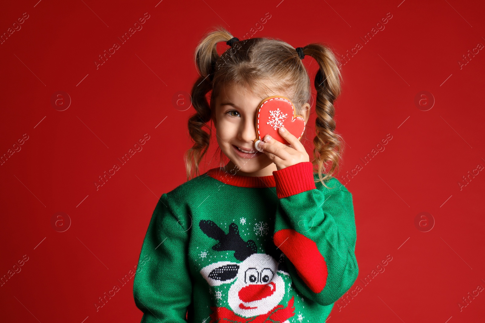 Photo of Cute little girl with Christmas gingerbread cookie on red background