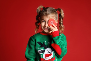 Photo of Cute little girl with Christmas gingerbread cookie on red background