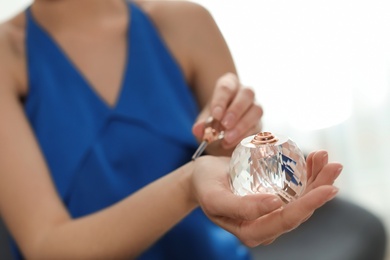 Photo of Young woman applying perfume on wrist against blurred background, closeup