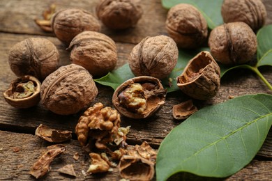 Photo of Whole and cracked walnuts with green leaves on wooden table, closeup
