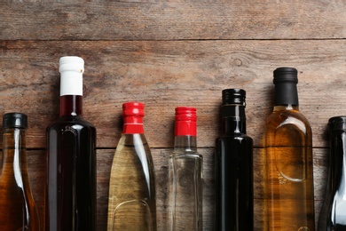 Bottles with different kinds of vinegar and space for text on wooden background, flat lay