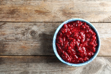 Bowl of tasty cranberry sauce on wooden background, top view. Space for text