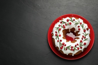 Photo of Traditional Christmas cake decorated with glaze, pomegranate seeds, cranberries and rosemary on dark grey table, top view. Space for text