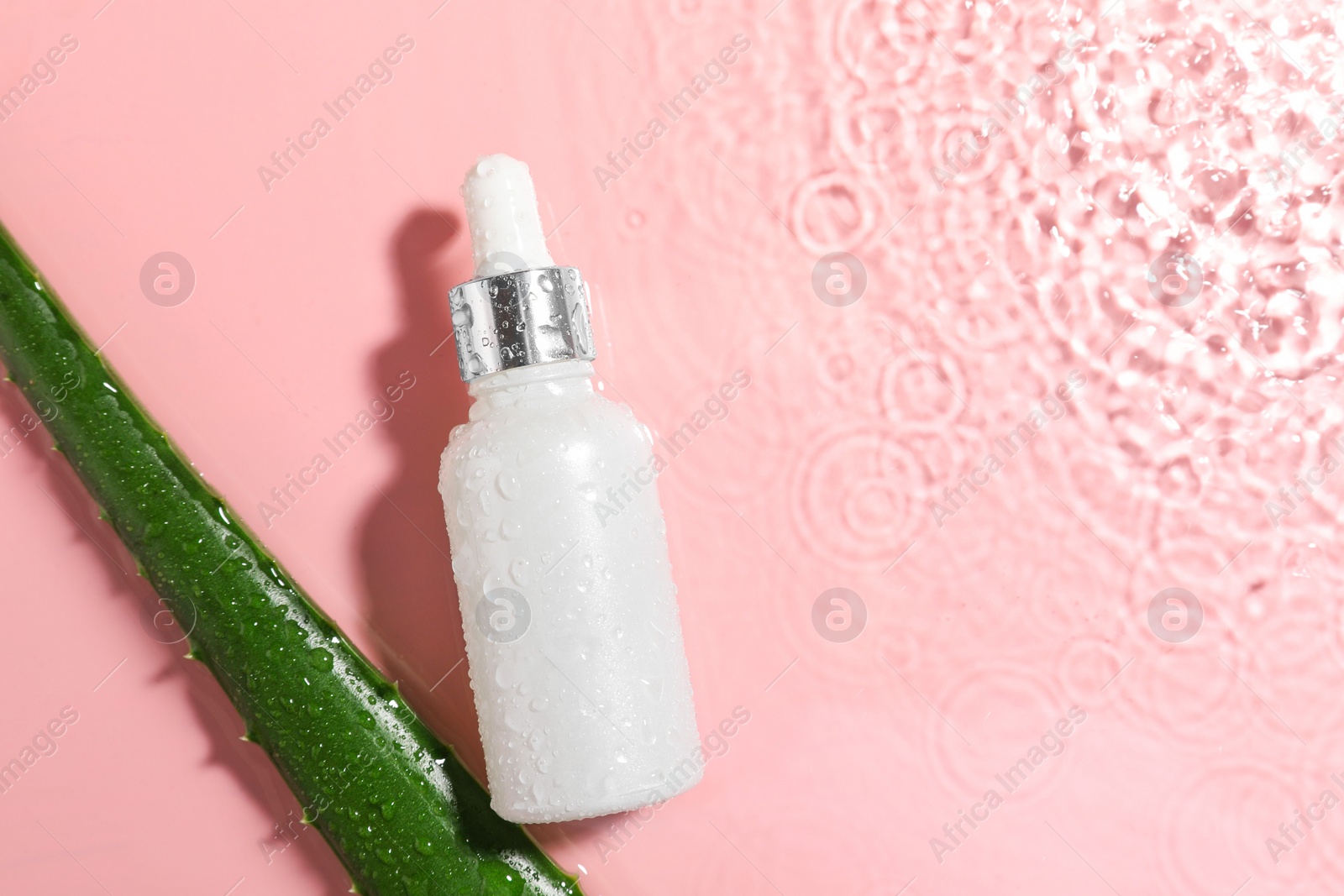 Photo of Bottle of cosmetic product and aloe leaf in water on pink background, flat lay. Space for text