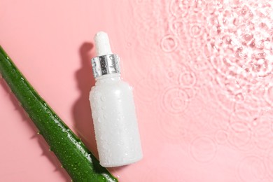 Bottle of cosmetic product and aloe leaf in water on pink background, flat lay. Space for text