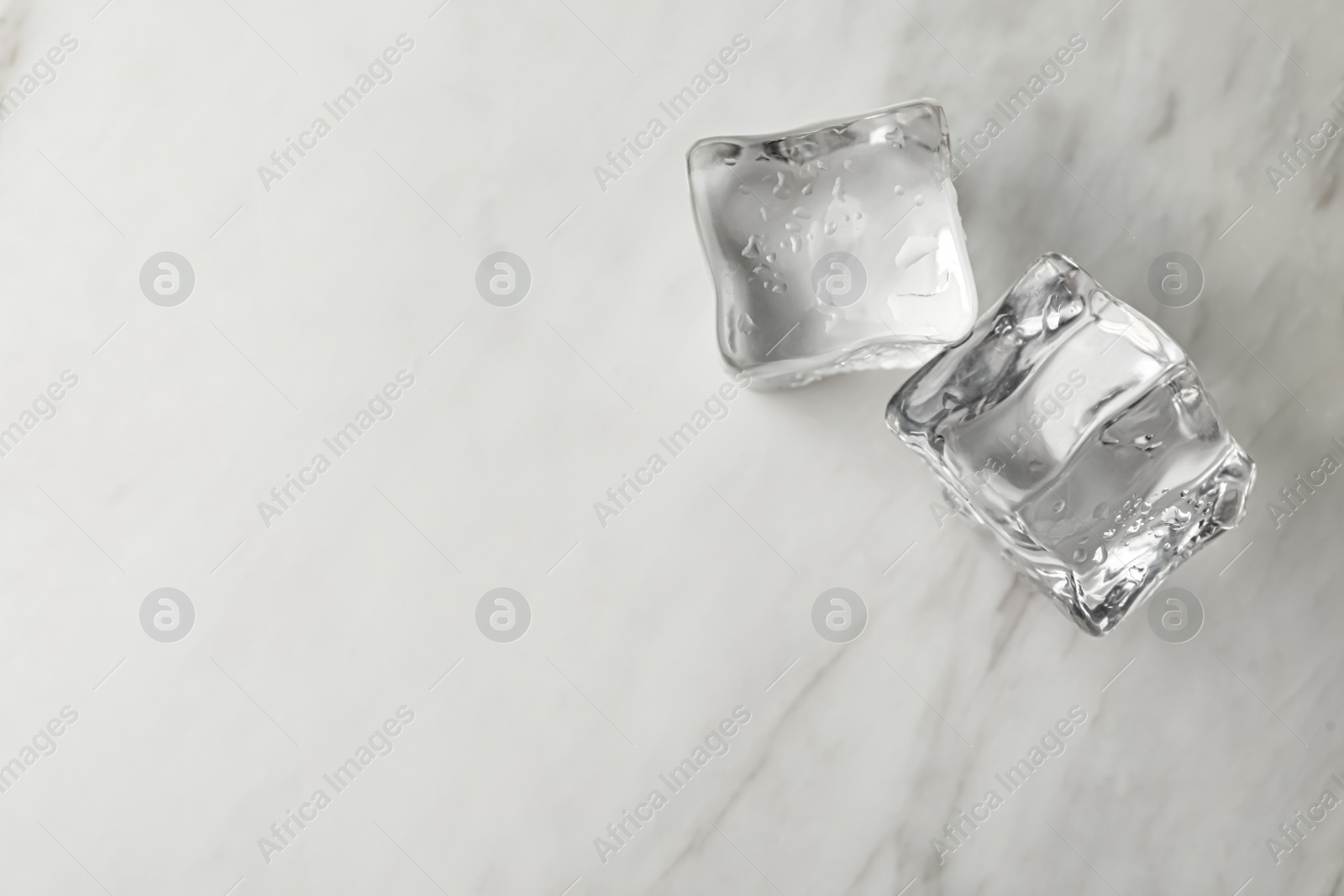 Photo of Crystal clear ice cubes with water drops on light table. Space for text