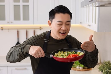 Man with frying pan smelling dish after cooking in kitchen