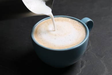 Photo of Pouring milk into cup of coffee on black table, closeup