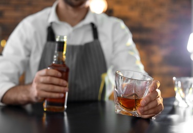 Photo of Bartender with glass and bottle of whiskey at counter in bar, closeup. Space for text