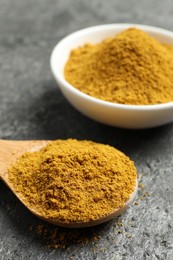 Photo of Spoon and bowl with dry curry powder on dark textured table, closeup