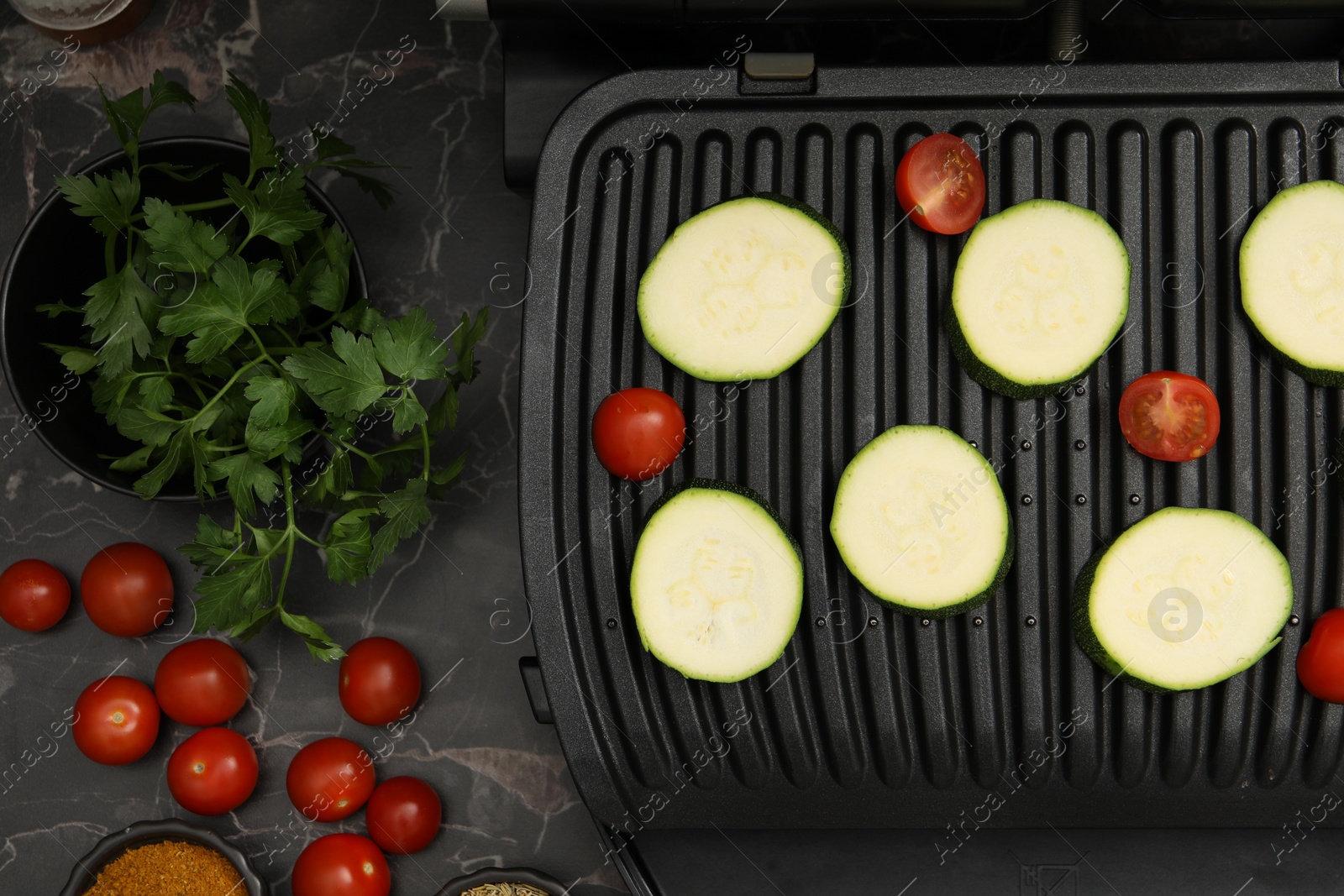 Photo of Electric grill with vegetables on black marble table, flat lay