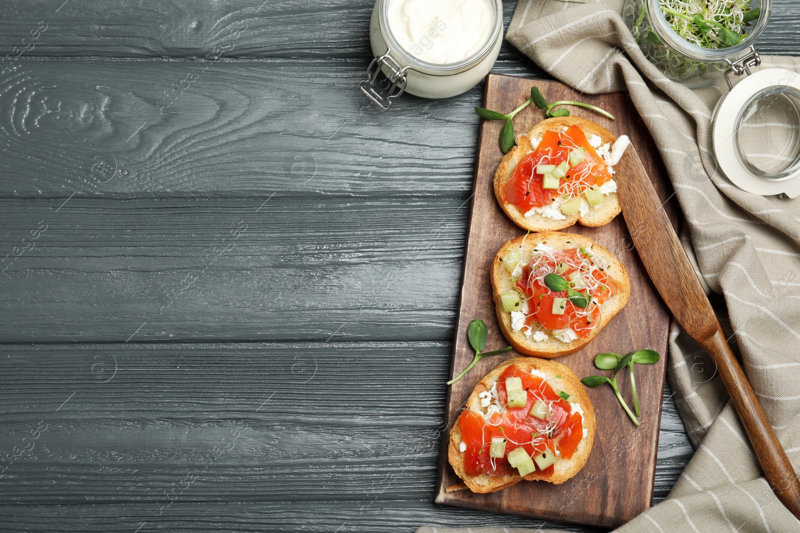 Photo of Flat lay composition of tasty bruschettas with salmon on dark grey wooden table. Space for text