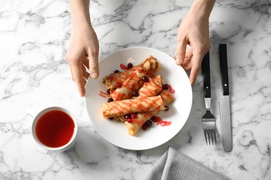 Woman putting plate with thin pancakes, berries and syrup on table, top view