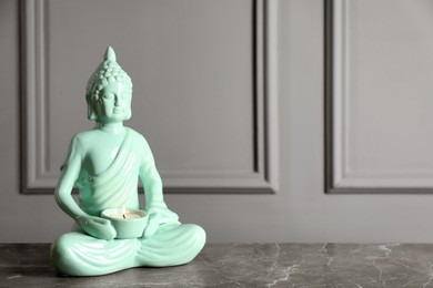 Photo of Buddha statue with burning candle on grey table. Space for text