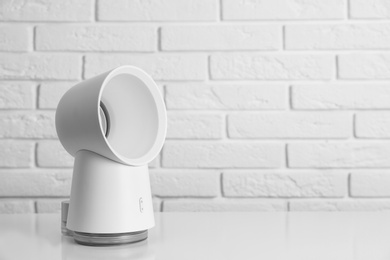 Portable fan on table near white brick wall, space for text. Summer heat