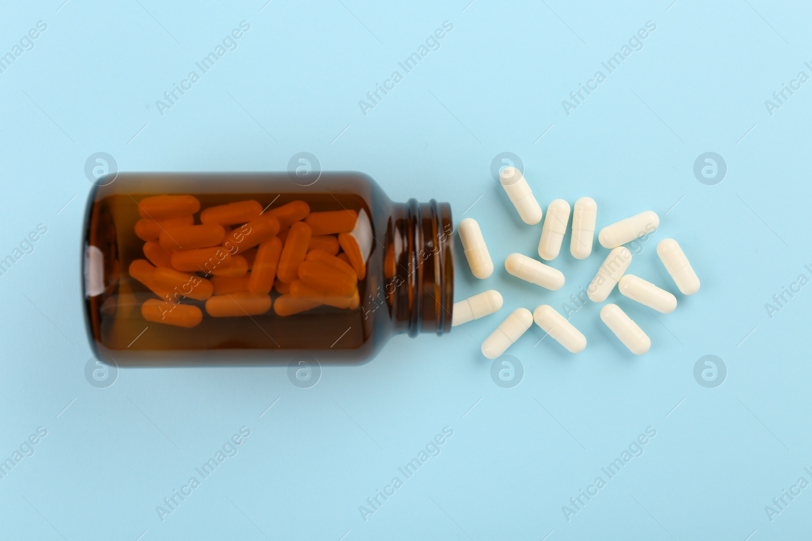 Photo of Bottle and vitamin capsules on light blue background, top view