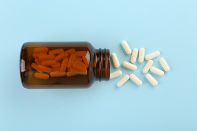 Bottle and vitamin capsules on light blue background, top view