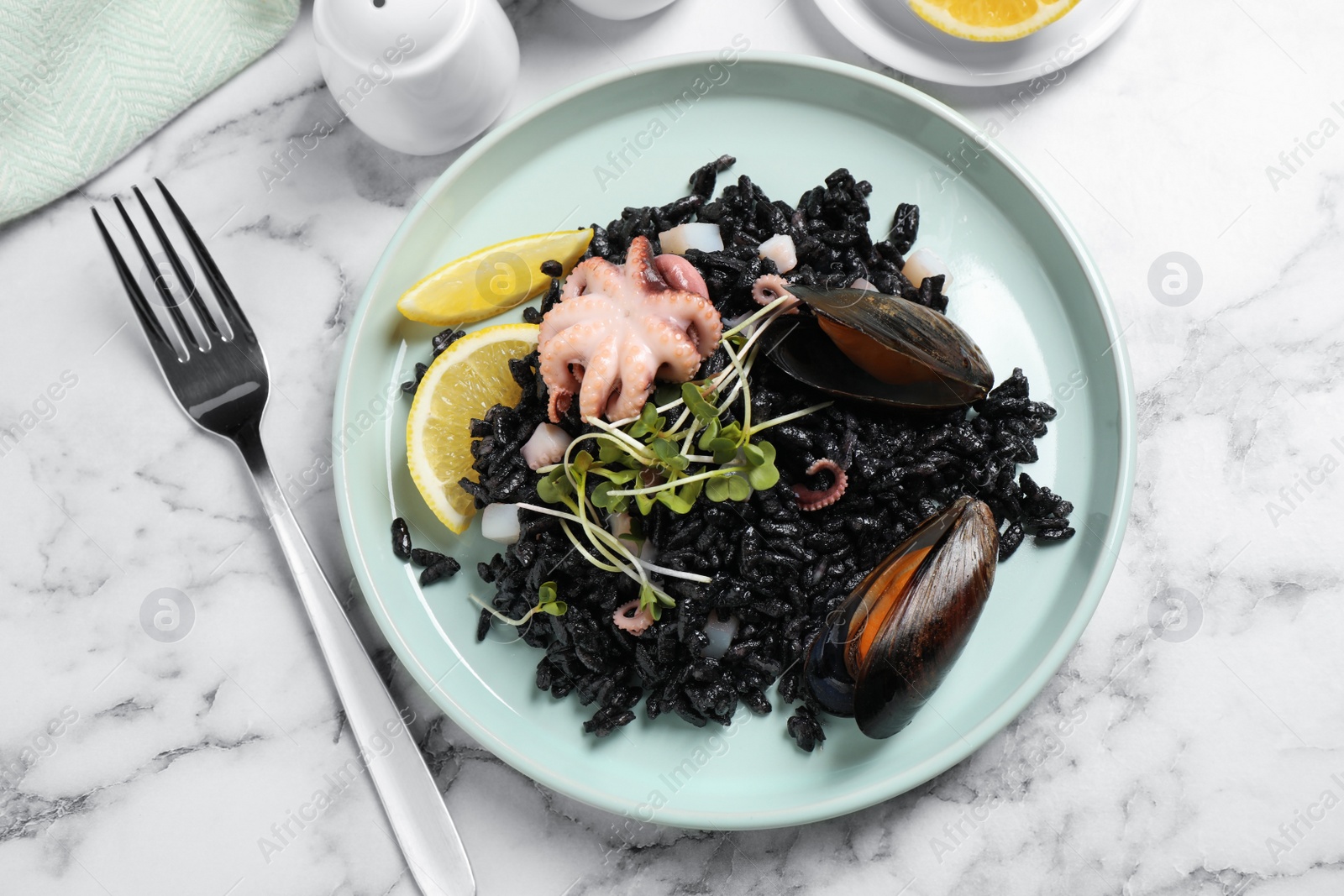 Photo of Delicious black risotto with seafood served on white marble table, flat lay