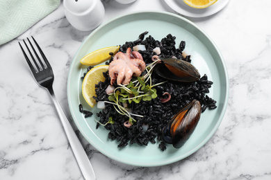 Photo of Delicious black risotto with seafood served on white marble table, flat lay