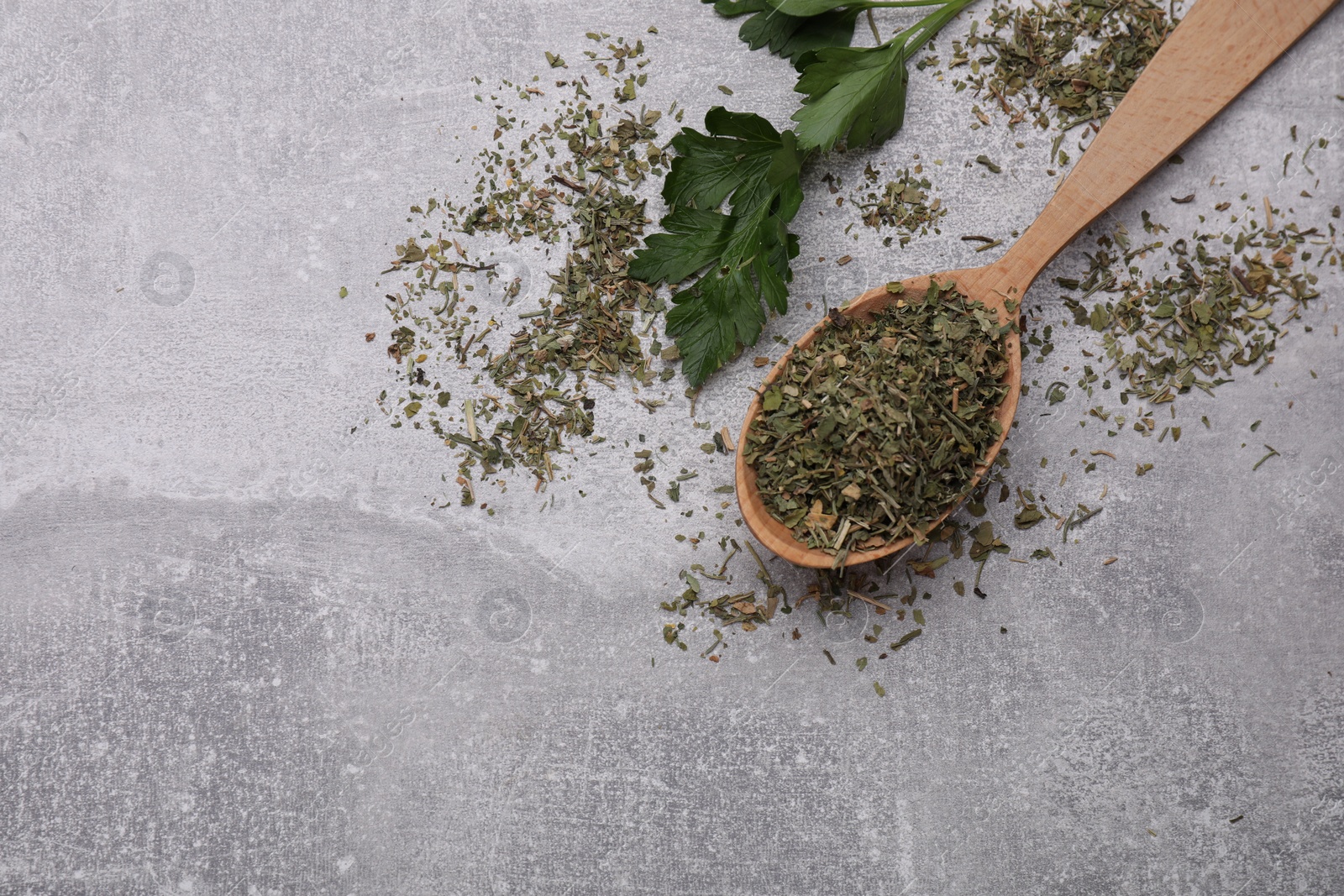 Photo of Wooden spoon with dried parsley and fresh leaves on light grey table, flat lay. Space for text