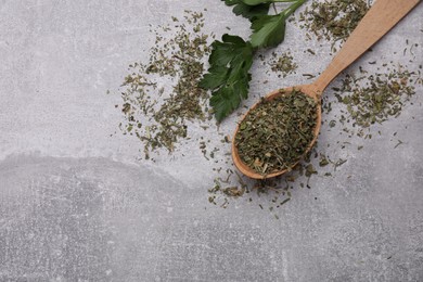 Wooden spoon with dried parsley and fresh leaves on light grey table, flat lay. Space for text