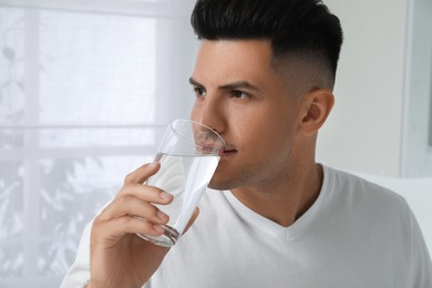 Man drinking tap water from glass at home, closeup