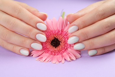 Woman with white polish on nails holding flower on violet background, closeup