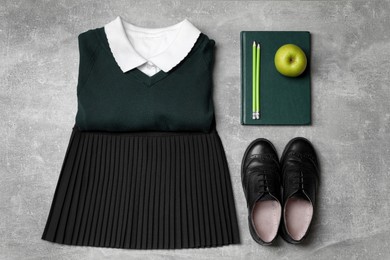 Stylish school uniform for girl, stationery and apple on grey background, flat lay