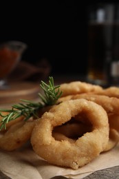 Photo of Pile of delicious crunchy fried onion rings with rosemary on wooden table, closeup