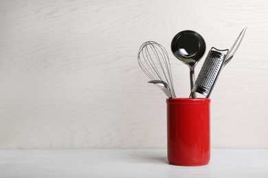 Photo of Holder with clean kitchen utensils on table. Space for text