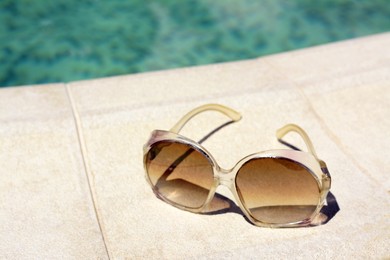 Photo of Stylish sunglasses near outdoor swimming pool on sunny day, closeup. Beach accessory
