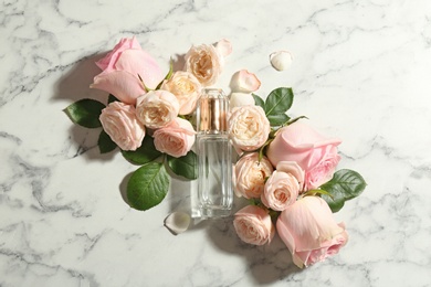 Beautiful composition with bottle of perfume and roses on marble background, top view