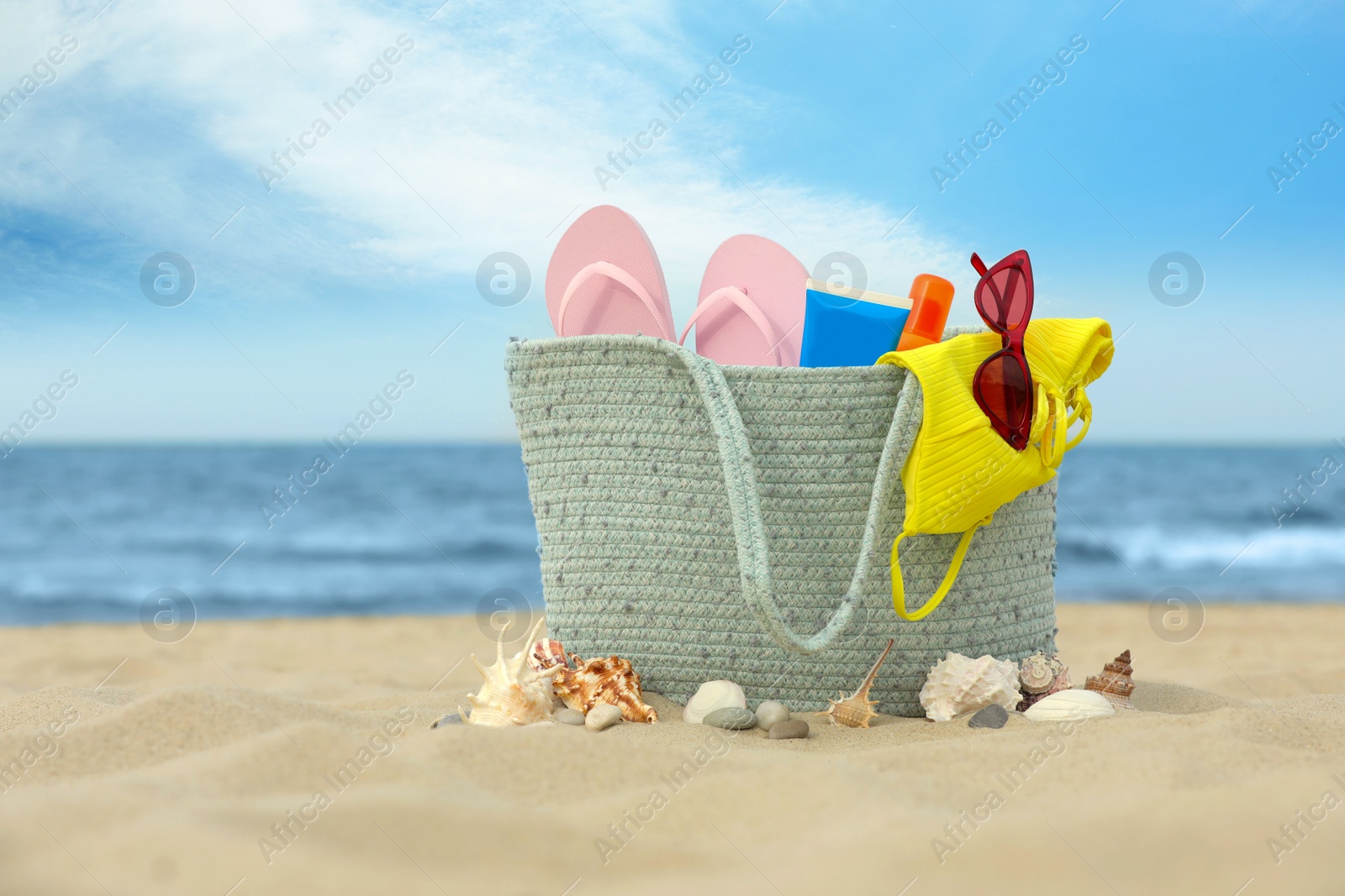 Photo of Bag with beach objects on sand near sea, space for text