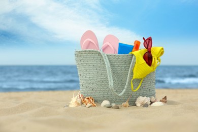 Photo of Bag with beach objects on sand near sea, space for text