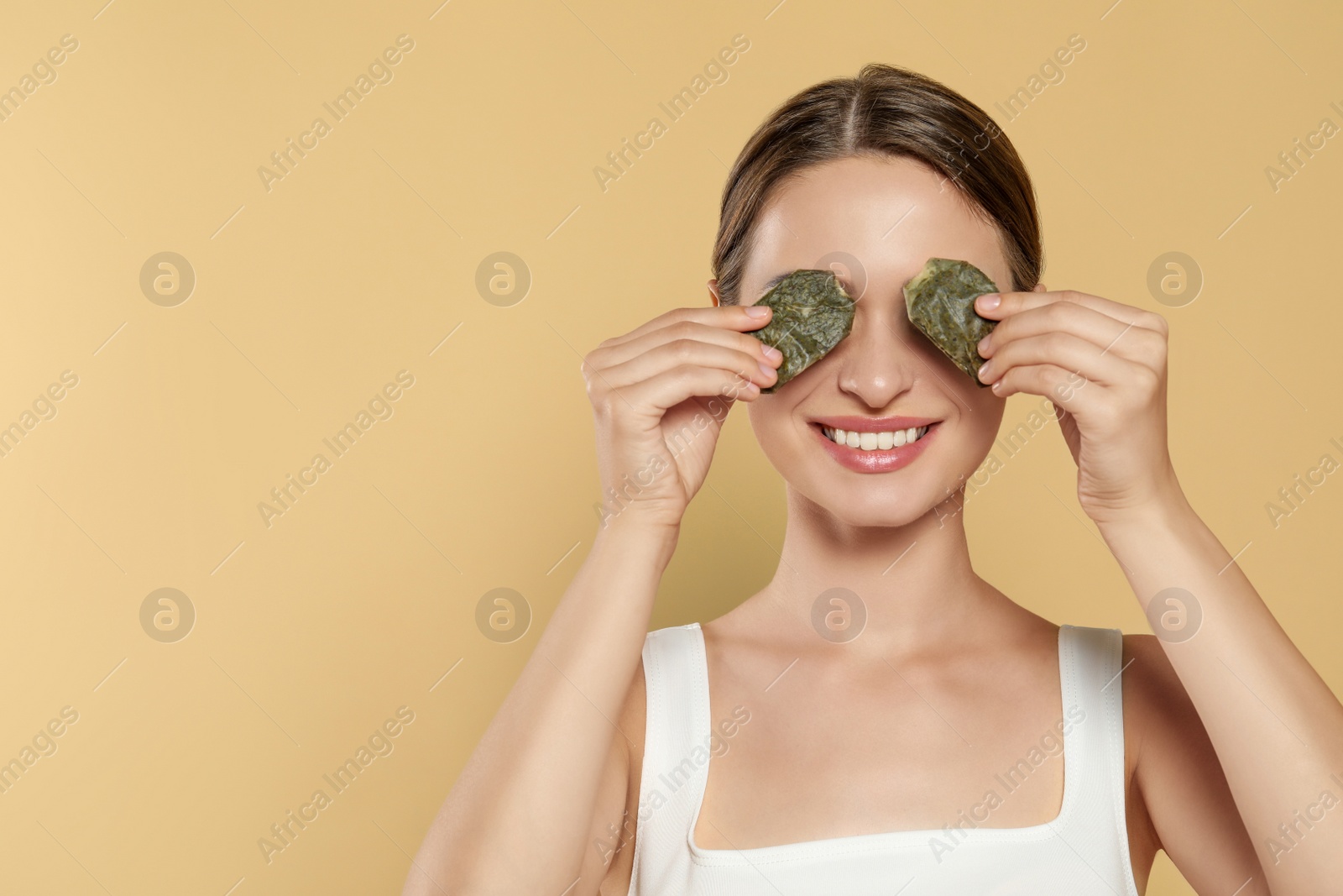 Photo of Young woman with green tea bags on beige background, space for text. Eye skin care