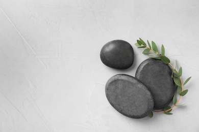 Photo of Black spa stones with eucalyptus on light background, top view. Space for text